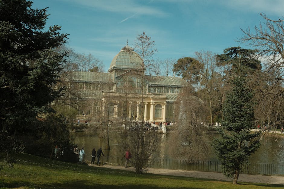 A large, historic glass-domed conservatory with classical architectural details, situated beside a reflecting pond. The building features a prominent central dome with a decorative spire, flanked by s